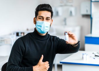 modern-indian-man-holds-vaccine-his-hands-smiles-wearing-protective-mask_496169-2910